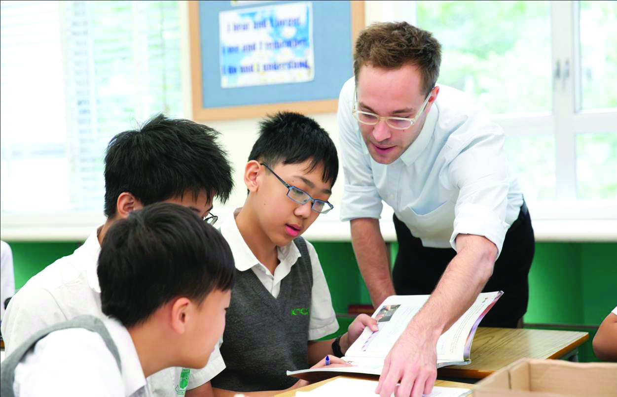 a male TEFL teacher is showing explaining a task in English to Chinese students